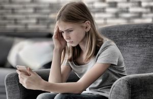 Sad teenage girl with smartphone at home